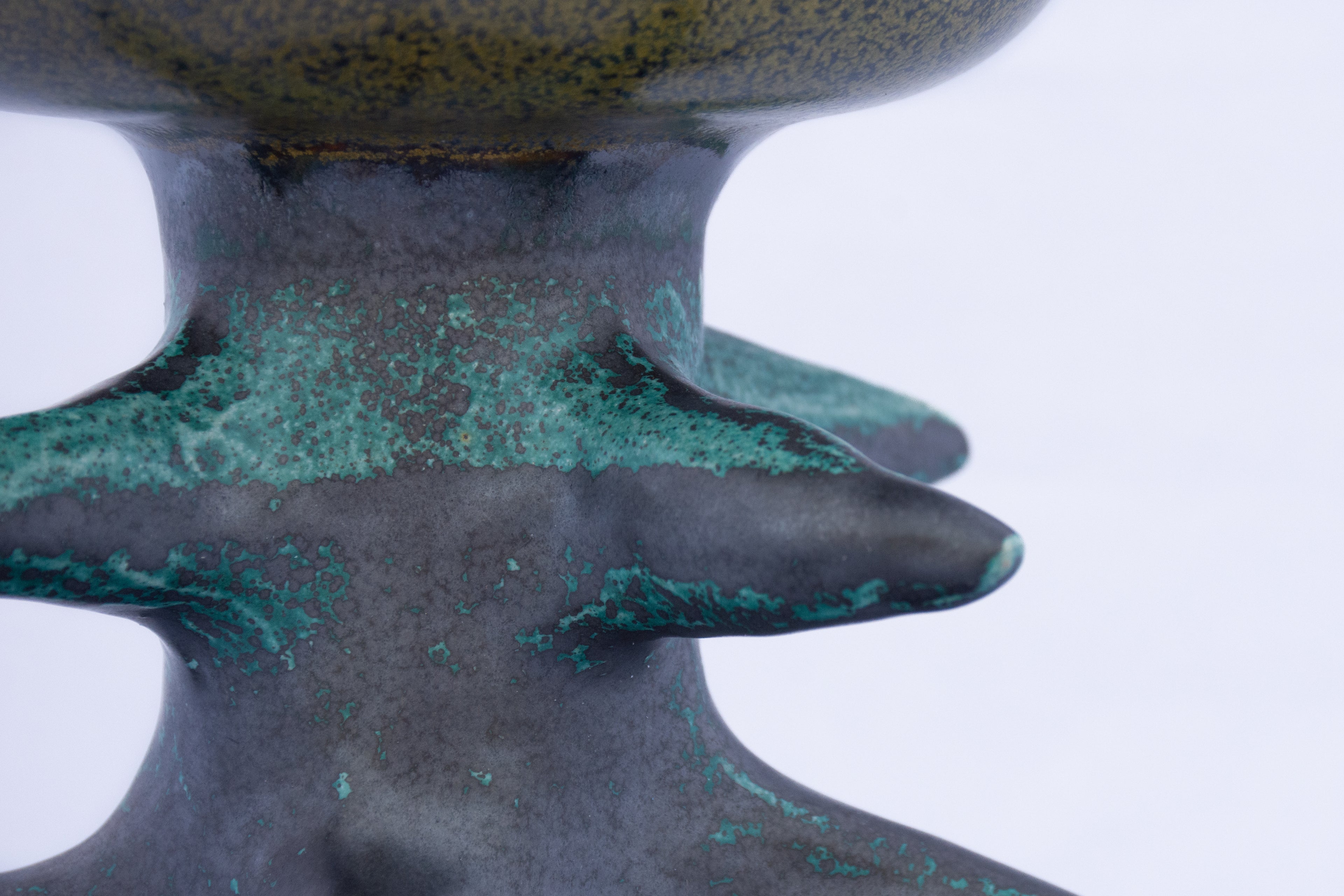 Close-up of a textured ceramic object with green and black coloration on a white background