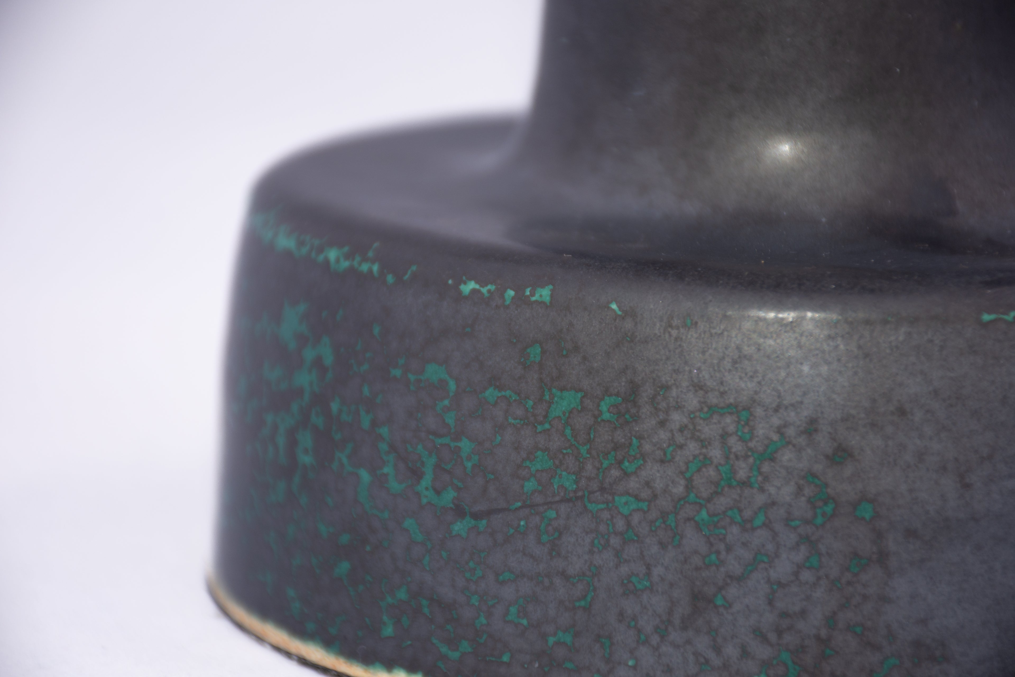 Close-up of a dark ceramic lamp base with green speckles on a white background